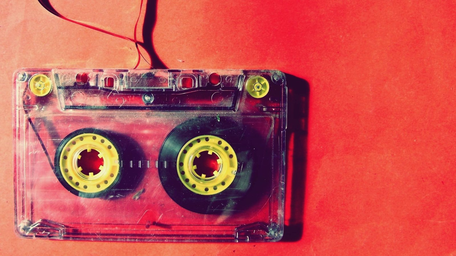 Transparent cassette tape with yellow hubs on a red background.